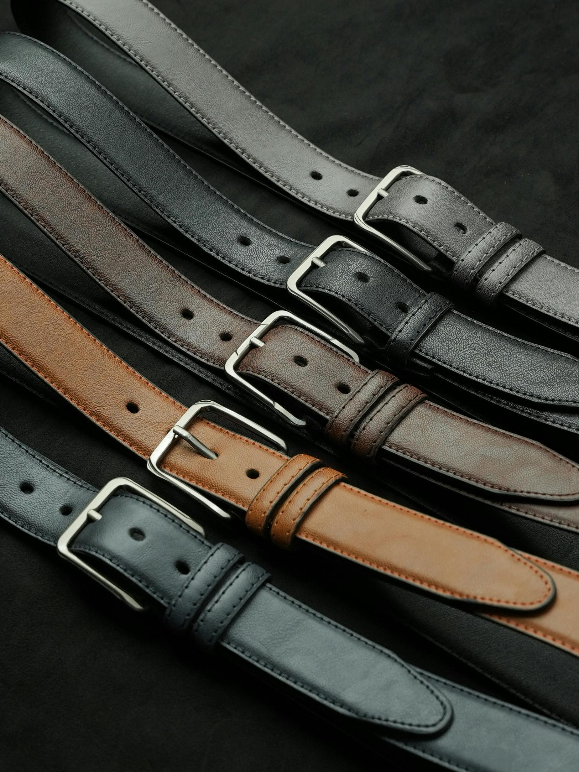 A variety of leather belts in different colors and styles, displayed on a dark background.